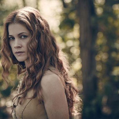 She has her long red head with blurry forest background.